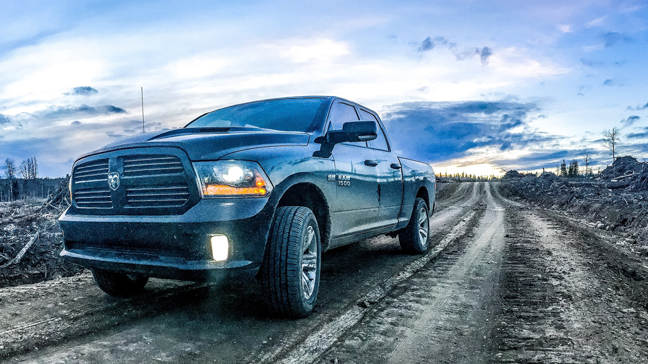 Ram 1500 with headlights on at dusk driving down a dirt road in a rural area