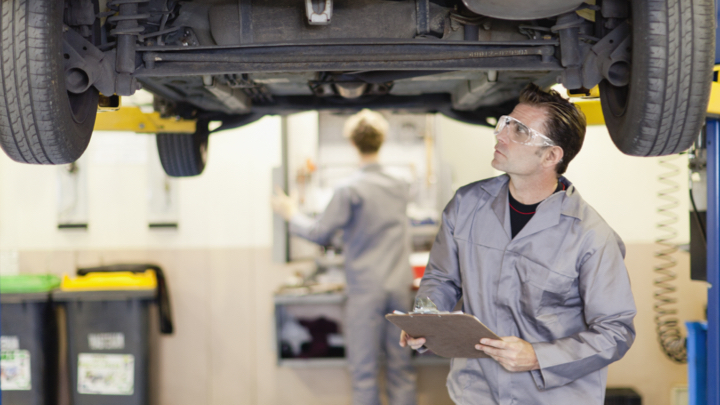 Technician with clipboard inspecting under vehicle