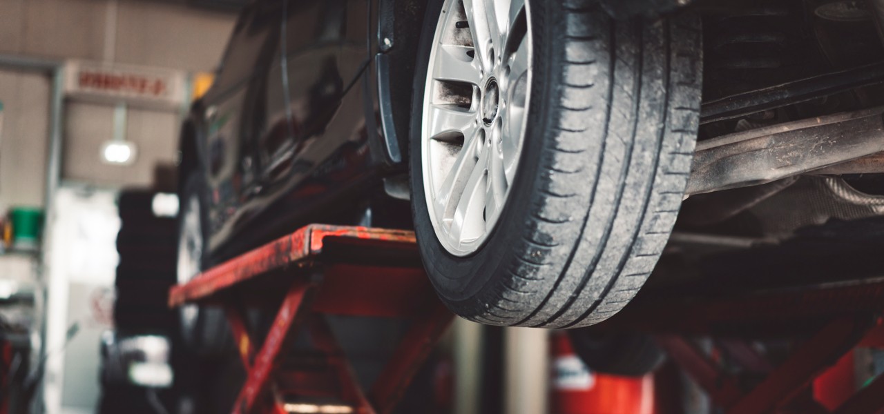 why-do-tires-wear-unevenly-hero Car on lift with focus on tire.